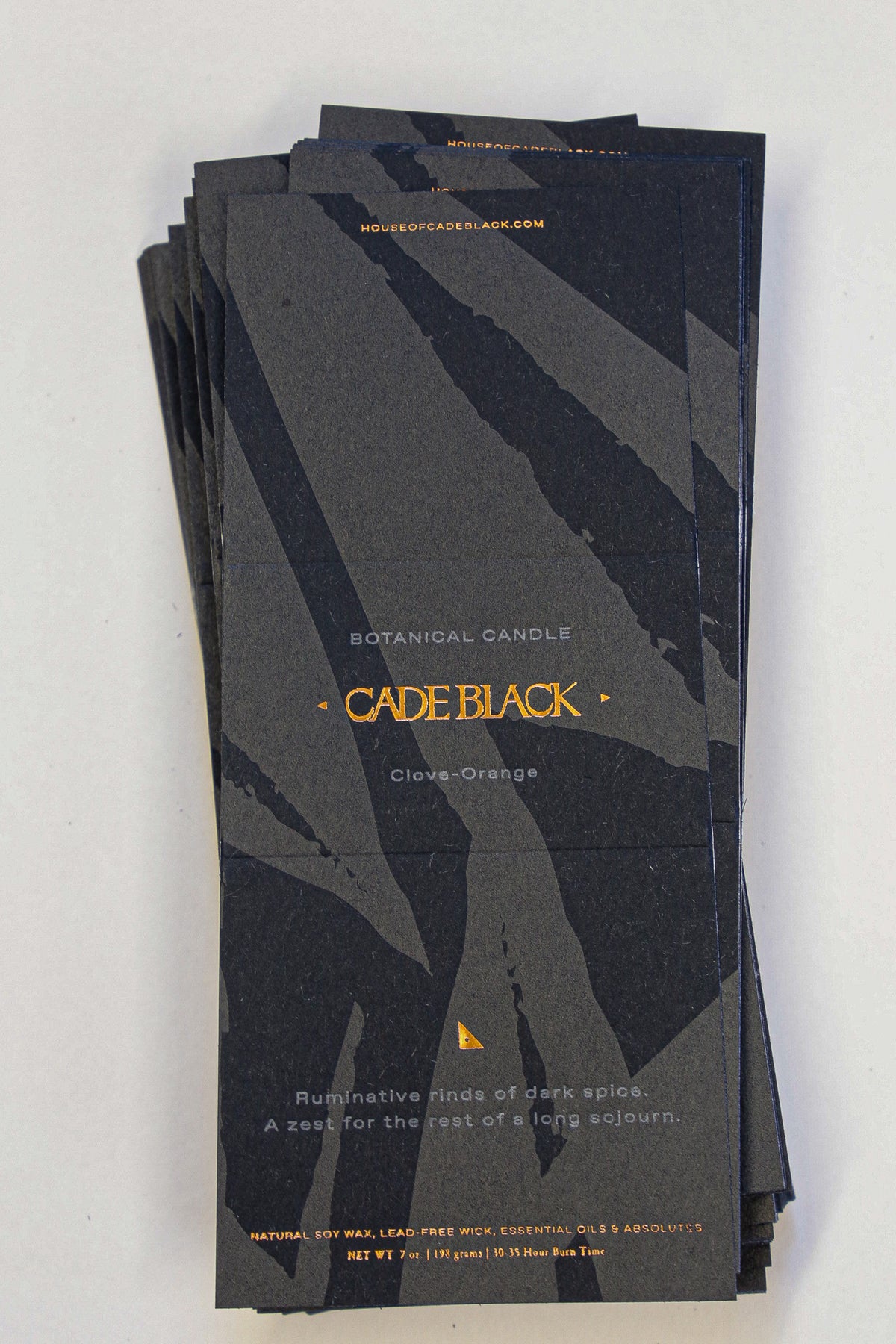 Stack of black candle packaging with gold text on a white background